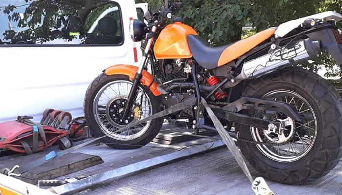 Motocicleta laranja presa por cintas sobre uma plataforma metálica.