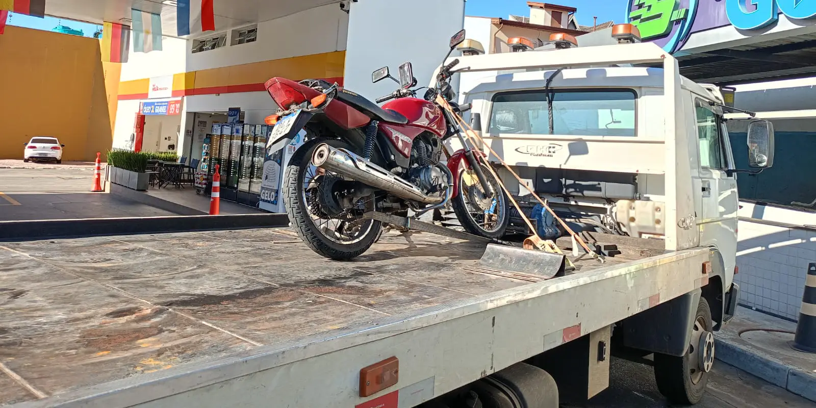 Motocicleta vermelha presa por cintas sobre a plataforma do guincho.