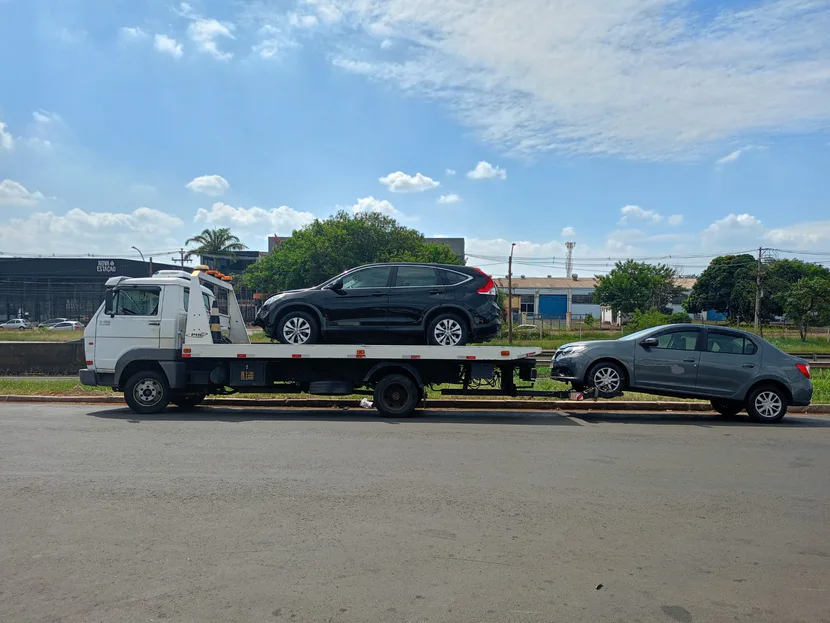 Caminhão de guincho com um SUV escuro sobre a plataforma, visto do outro lado da rua.