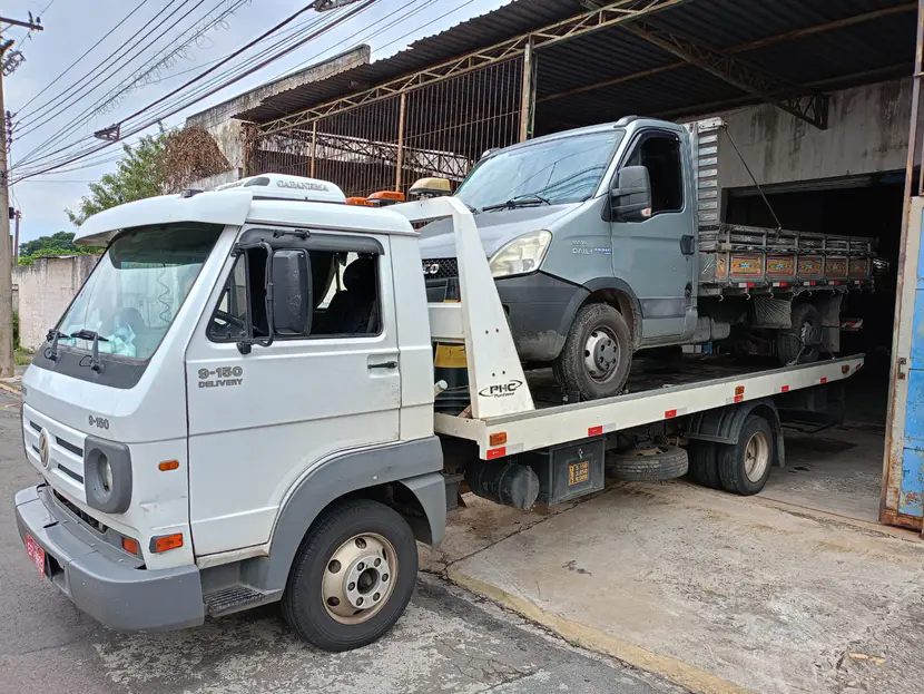 Caminhão leve cinza sobre a plataforma do guincho diante de um galpão.