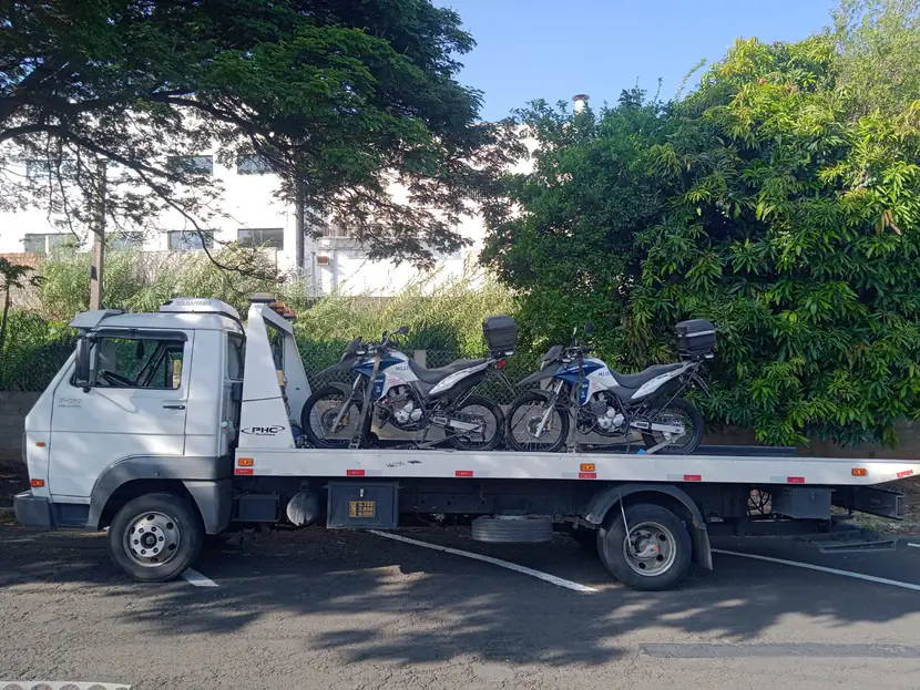 Duas motocicletas sobre a plataforma do caminhão, sob árvores.