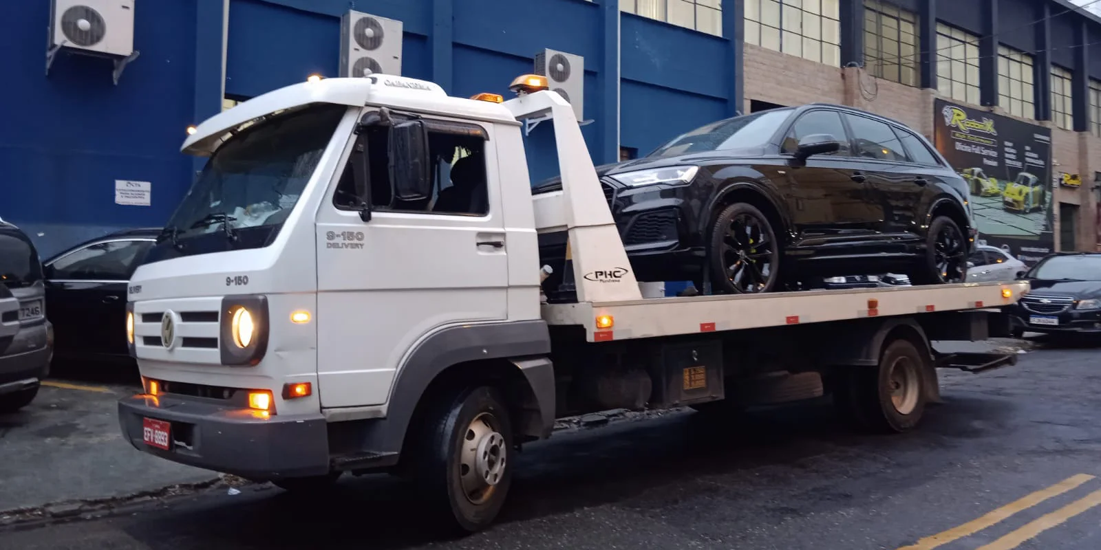 SUV preto sobre a plataforma do guincho diante de um prédio azul.