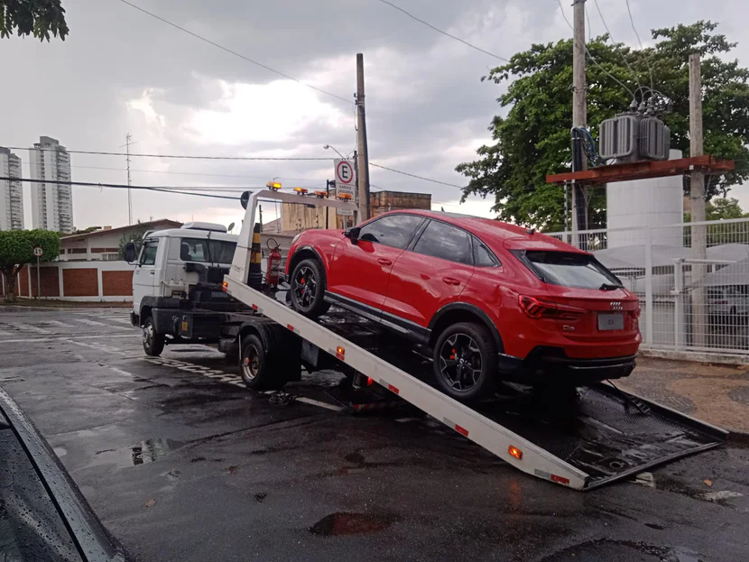 SUV vermelho sobre a plataforma inclinada de um caminhão de guincho.