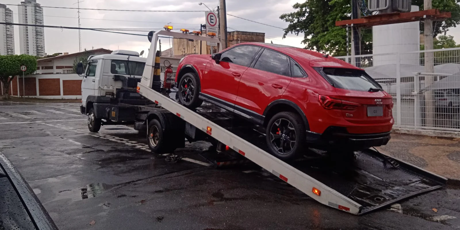 SUV vermelho sobre a plataforma inclinada de um caminhão de guincho.