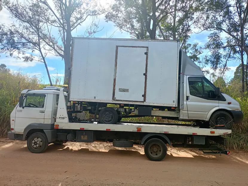 Utilitário branco com baú sobre a plataforma do caminhão, sob árvores.
