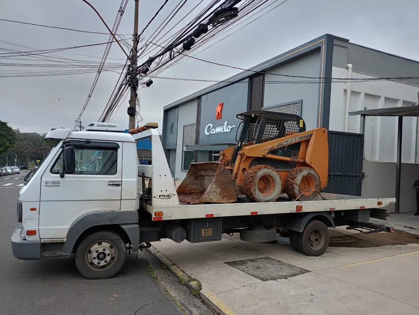 Minicarregadeira amarela sobre a plataforma do caminhão diante de um prédio.