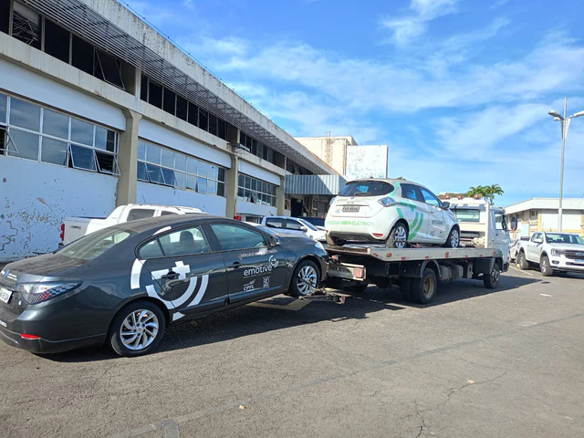 Carro branco sobre a plataforma do guincho, ao lado de carros estacionados.